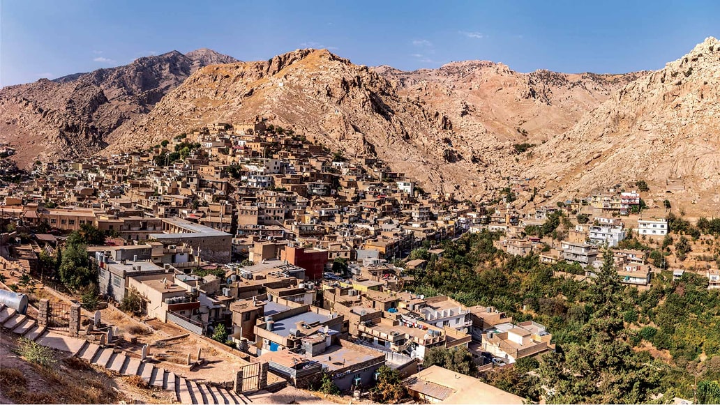 Aerial image of an Iraqi city nestled beside rocky hills under a clear blue sky