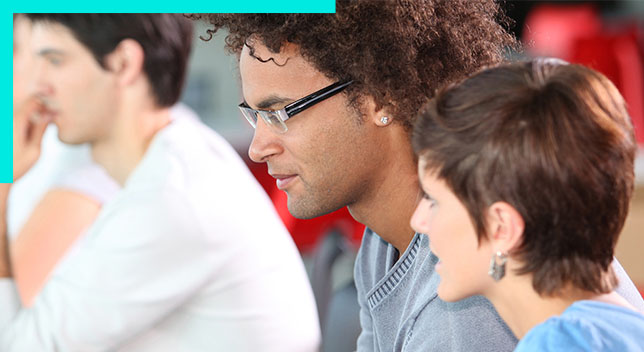 Photo of three casually dressed attendees in a group seminar setting gazing to the left at an unseen speaker or screen