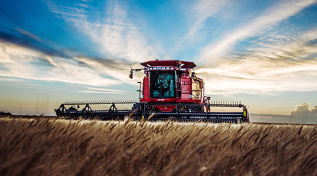 A photo of a red combine harvester in a field of brown wheat under a blue sky streaked with white clouds
