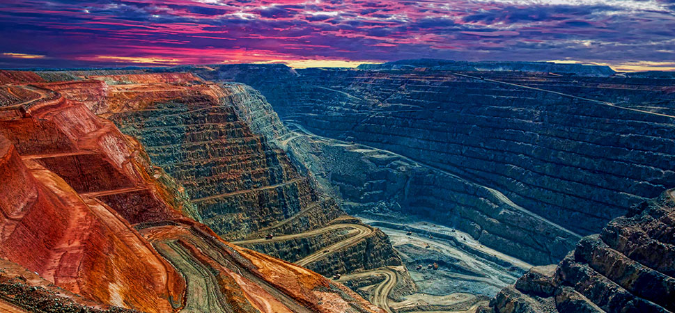 A colorful mining quarry landscape of a mining quarry with a purple and pink clouds on the horizon and trucks driving down the quarry roads to the bottom