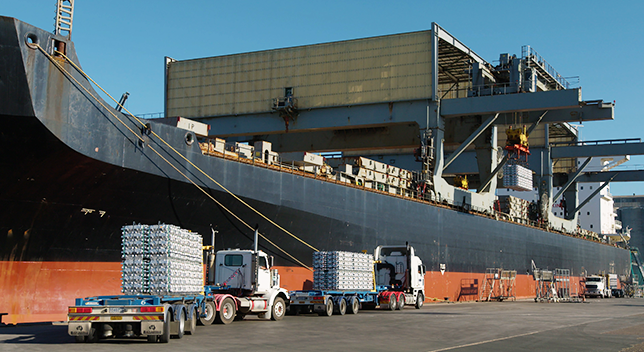 Trucks transporting cargo to a large shipping boat that is docked and loading