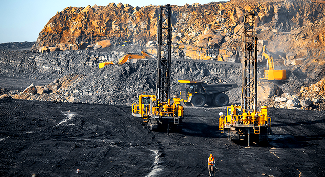 Drilling machines, bulldozers, and dump trucks work in a charred mine field 