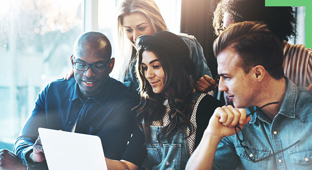 A group of coworkers huddled around a desk looking at a laptop