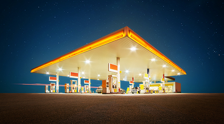 A brightly lit modern gas station in white and orange under a deep blue night sky