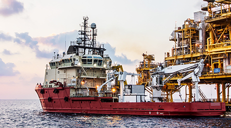 A platform supply vessel alongside an offshore oil rig on choppy blue waters under a pale sunrise sky
