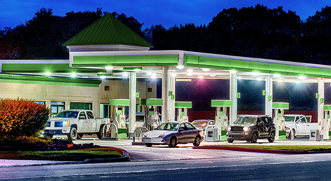 A gas station in green and white brightly lit against a dark blue twilight sky