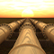 Three long massive white pipes stretch into the distance over a calm dull green ocean under an orange and yellow sunset 