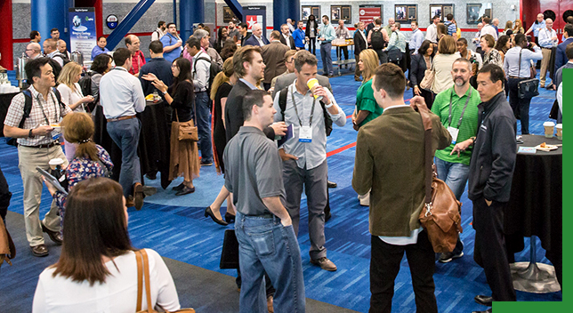 A photo of a crowded exhibit hall full of casually dressed attendees laughing and talking