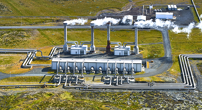 An aerial photo of a gray geothermal power plant in a wide green field