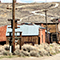 A dirt road winding through a mining town full of log cabins and brown desert scrub