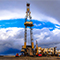 A photo of an oil rig surrounded by utility workers and vehicles with a cloudy blue sky in the background