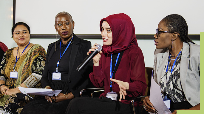 Four people sitting side-by side with one speaking into a microphone