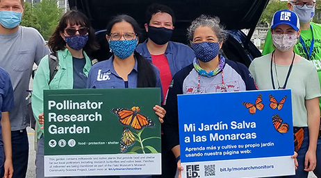 A photo of a group of casually dressed people in face masks holding green and blue exhibit signage