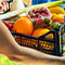A photo of a pair of hands passing a basket of produce to another pair of hands with an unfocused sunlit field in the background
