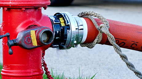 A closeup photo of a red fire hydrant connected to a red hose with a sparkling blue river in the background