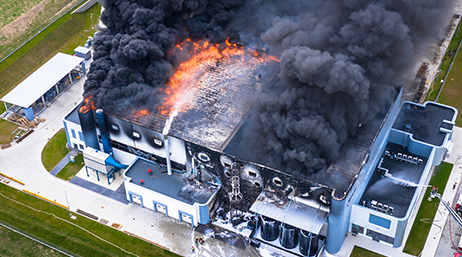 An aerial photo of a large administrative building surrounded by a green field, engulfed in flame and billowing black smoke