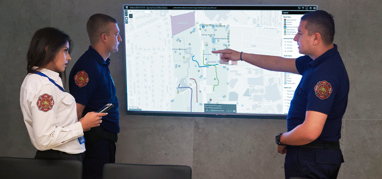 Three firefighters looking at a large screen with a map on it