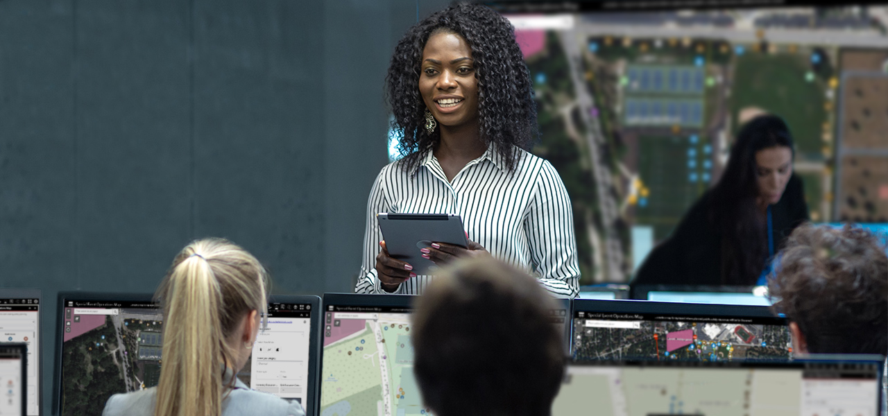 Person holding a tablet and looking at two people seated at desktop computers