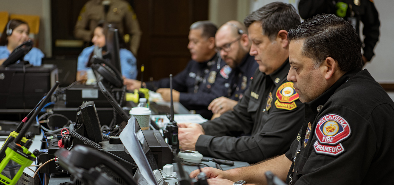 Vigili del fuoco di Pasadena seduti davanti a tavoli con telefoni, radio ricetrasmittenti e computer