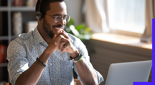 Personne portant des lunettes, assise à son bureau, souriante et regardant un écran d’ordinateur portable