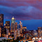 A wide view photo of Seattle, Washington lit up in sunset shades of gold and blue against an overcast twilight sky of dark blue and pink