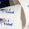 A closeup photo of a roll of stickers printed with a red and blue US flag and the words “I Voted”