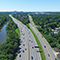 An aerial view of a highway surrounded by trees and a river with a city in the background