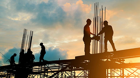 Construction workers on top of a building structure with a sunset in the background