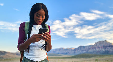A person wearing a backpack holding a phone with mountains in the background