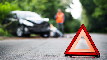 A roadside emergency triangle in front of a damaged car on the shoulder of the road