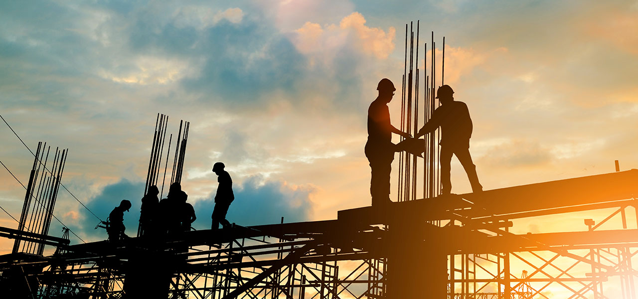 Trabalhadores da construção civil em cima de uma estrutura de construção com um pôr do sol ao fundo