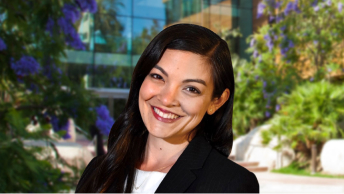 Portrait of Michelle Tateyama wearing a dark suit and smiling with Esri’s headquarters building in the background