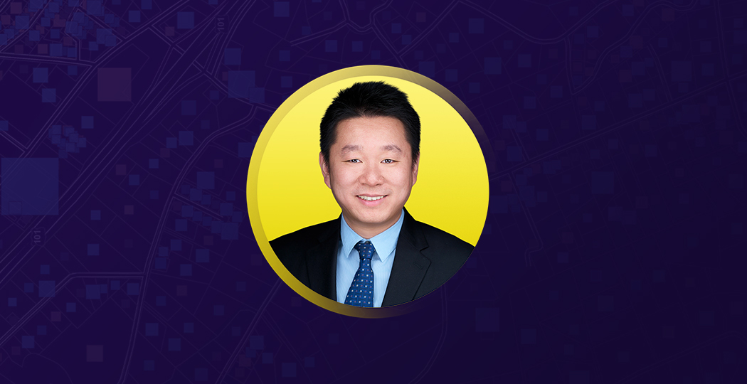 Yu Sun smiling in business attire on a yellow and purple background