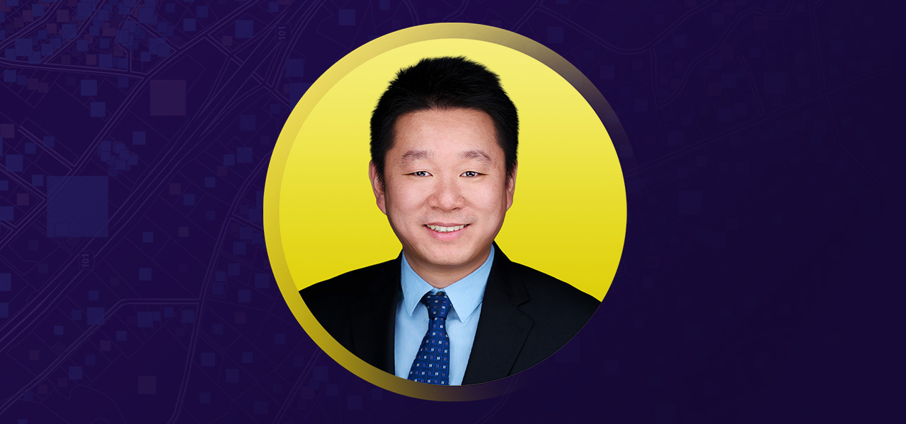 Yu Sun smiling in business attire on a yellow and purple background