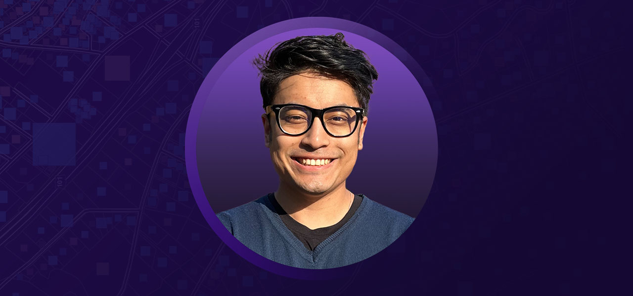 Ayush smiling in a black and navy blue shirt overlaid on a purple background