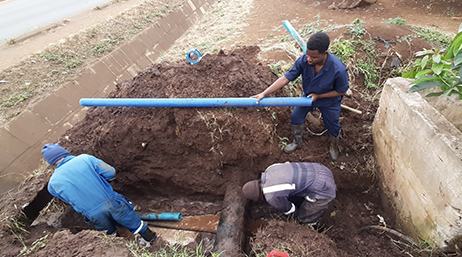 Three workers repairing a pipe in the ground