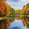 A rippling river reflecting the vivid autumn-colored trees along both banks beneath a hazy blue sky