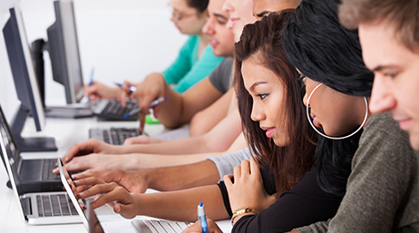 Студенты колледжа сидят за ноутбуками и мониторами в ярком современном компьютерном классе