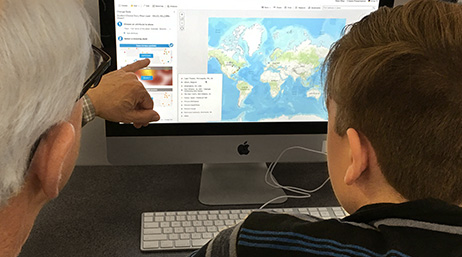 A teacher gestures to a digital map on a computer monitor as a student looks on