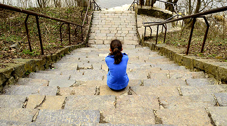 A photo from the top of an outdoor staircase with a single student seated halfway down, wearing a vivid blue shirt
