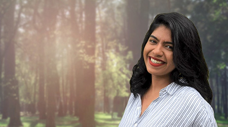 A smiling person in a white collared shirt with a sunlit forest in the background