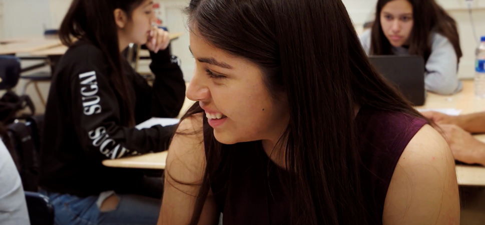A screencap from the featured video showing a laughing student with a classroom full of other students visible in the background
