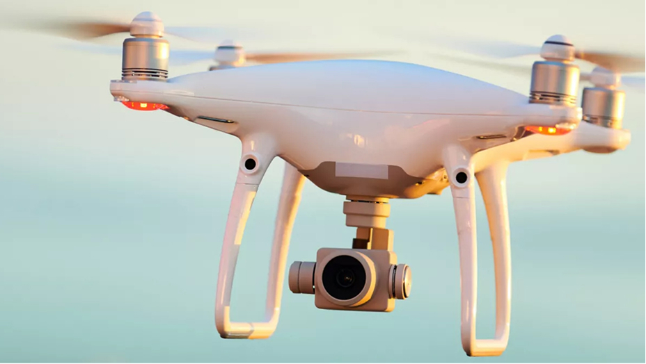 A closeup photo of a sleek white drone in mid-flight against a soft-focus pale blue sky