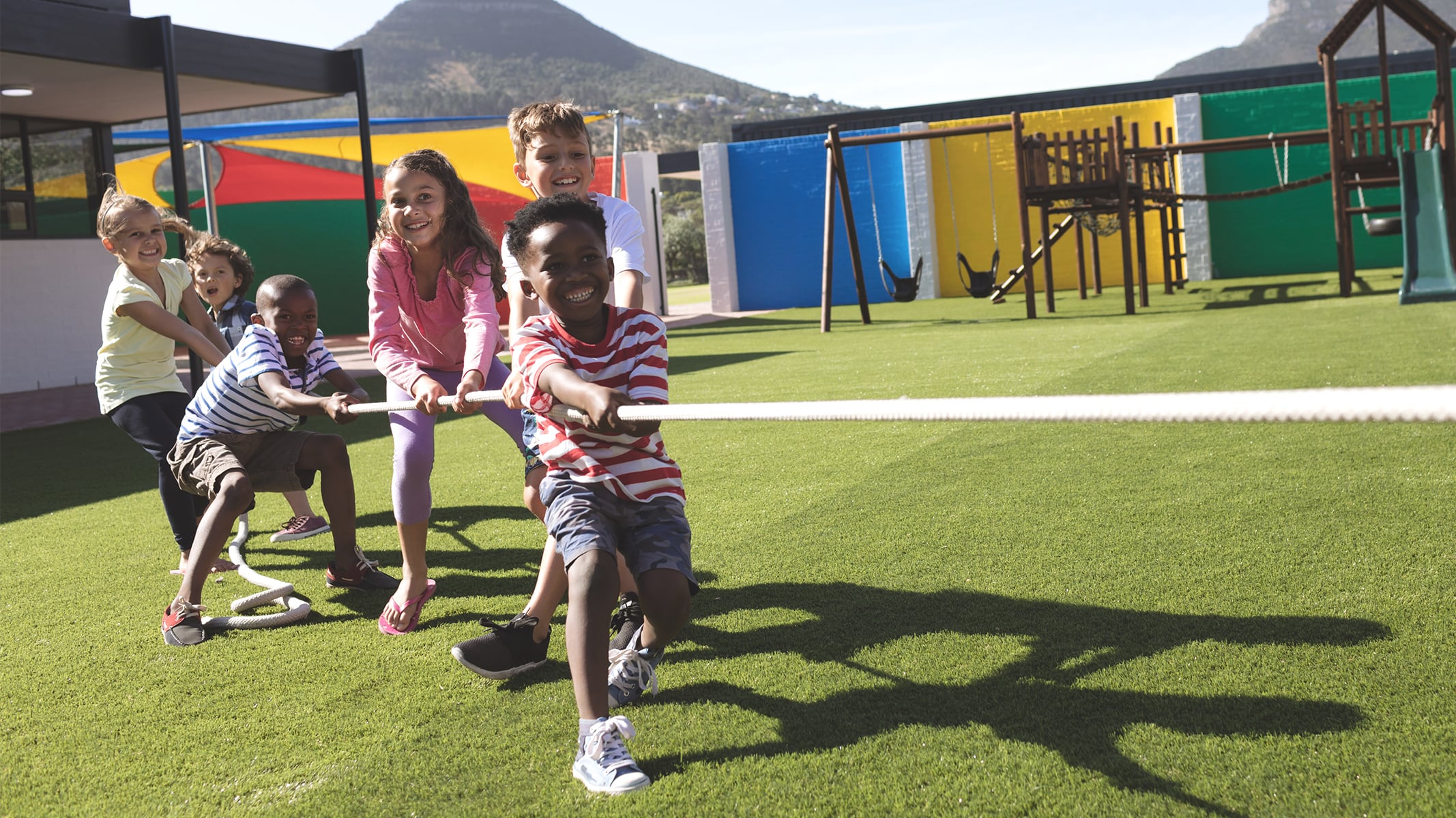 A group of students laughing as they play tug of war on a colorful sunlit playground