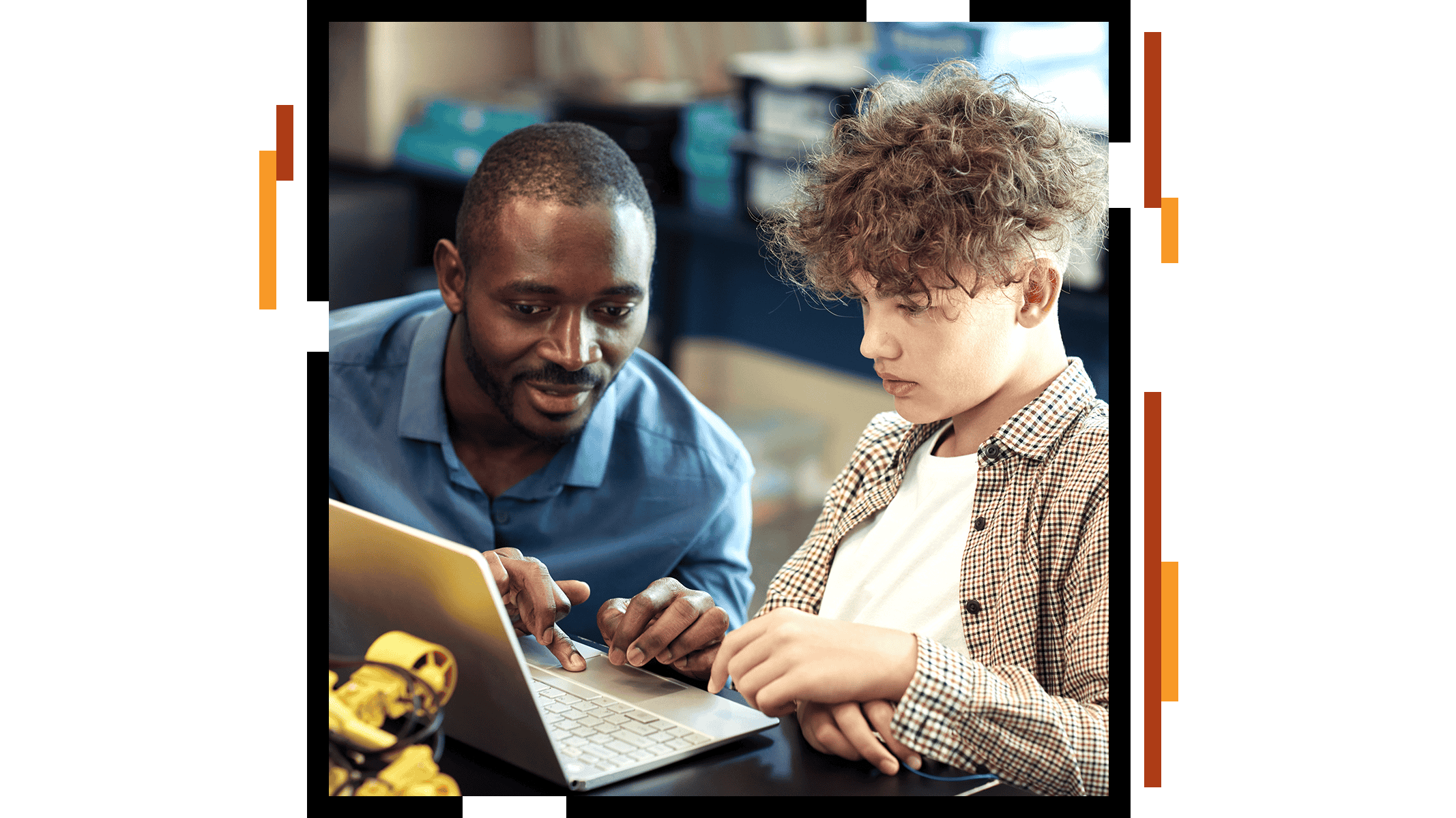 Ein Lehrer in einem blauen Hemd mit Kragen, der einem Schüler an einem aufgeklappten Laptop in einem hellen Klassenzimmer hilft