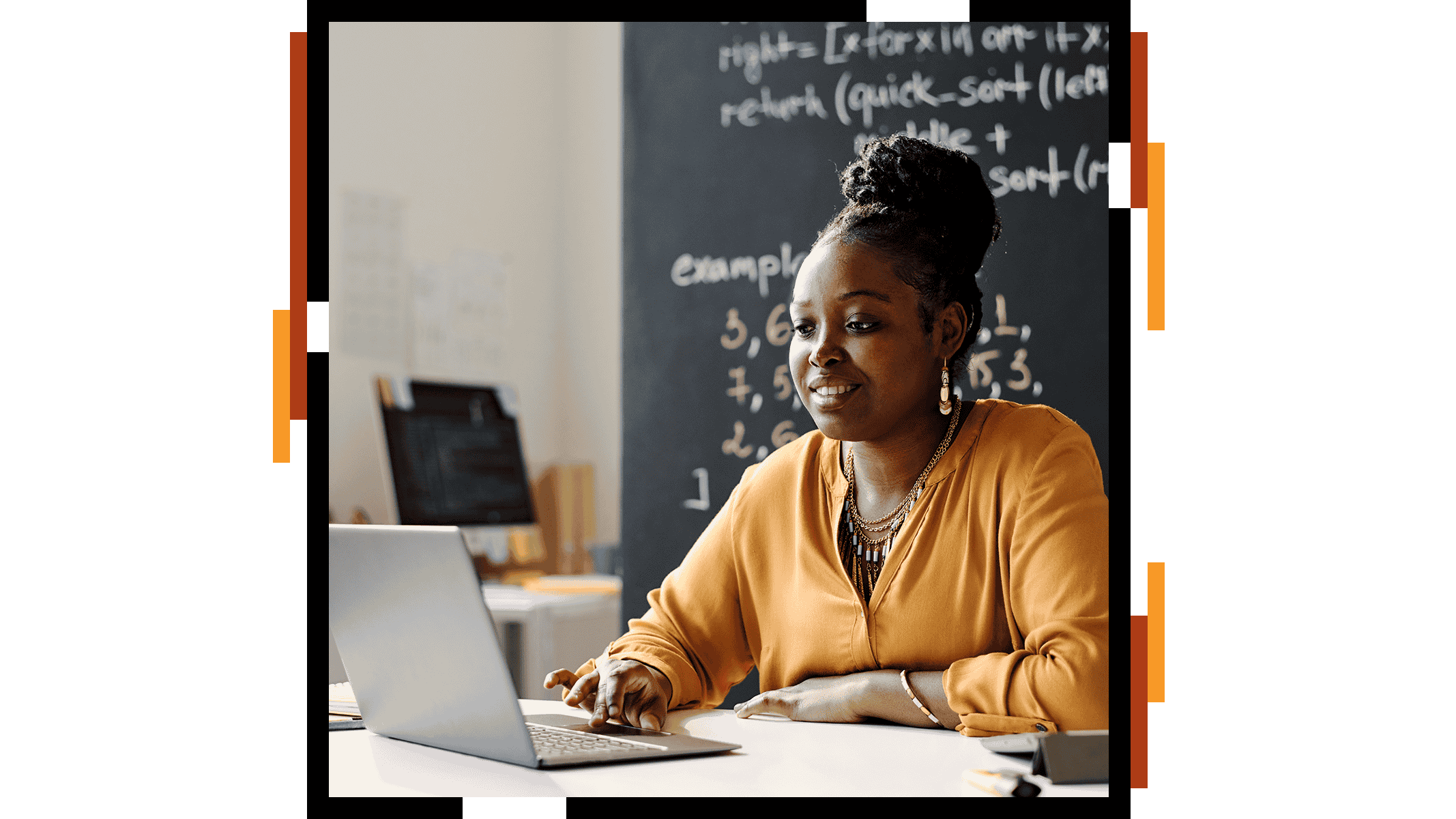 Eine lächelnde Lehrerin in einem gelben Pullover an einem aufgeklappten Laptop in einem sonnendurchfluteten Klassenzimmer
