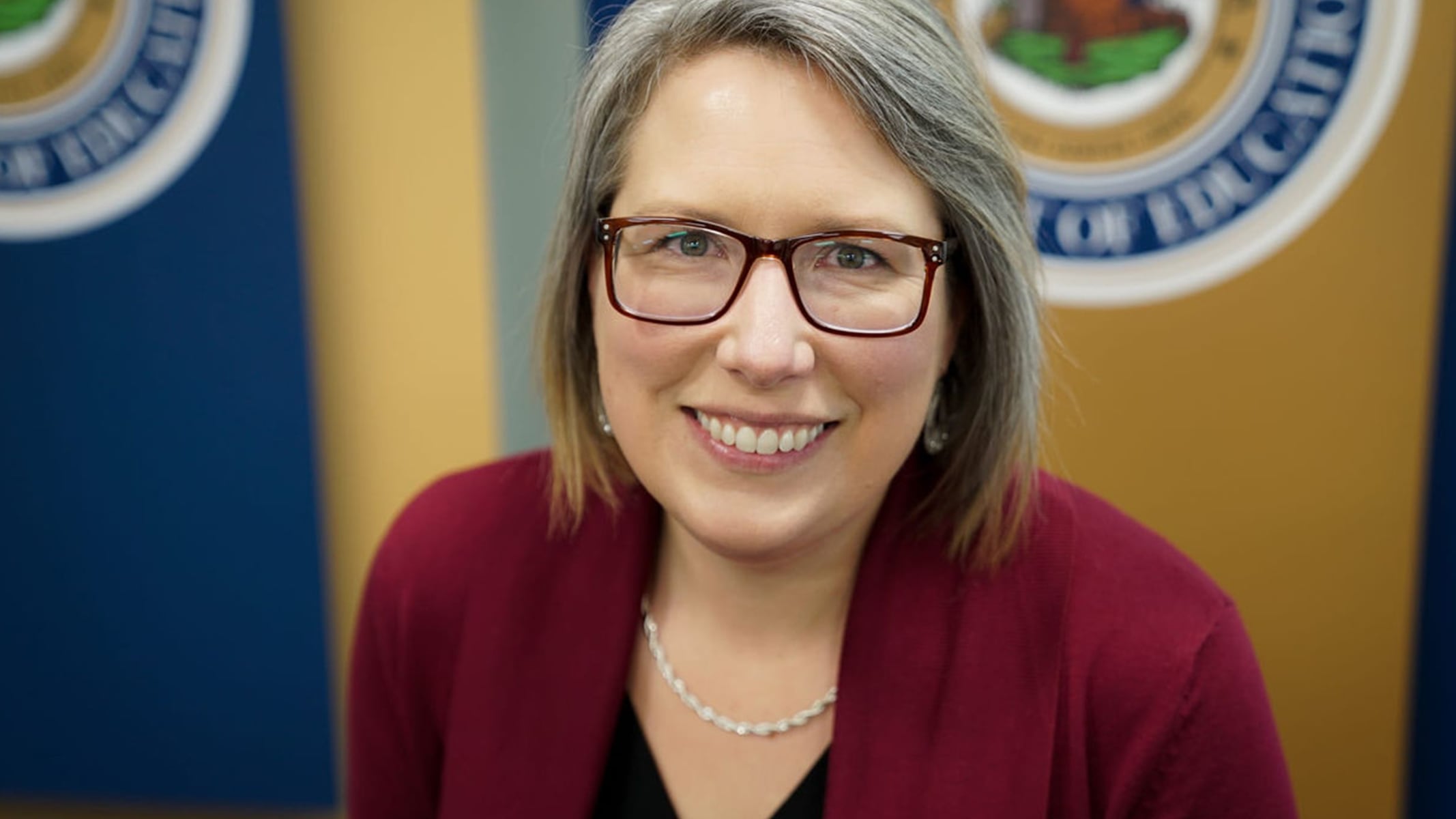 Dottor Klose sorridente, con un maglione bordeaux con un sigillo ufficiale del West Virginia Department of Education sullo sfondo