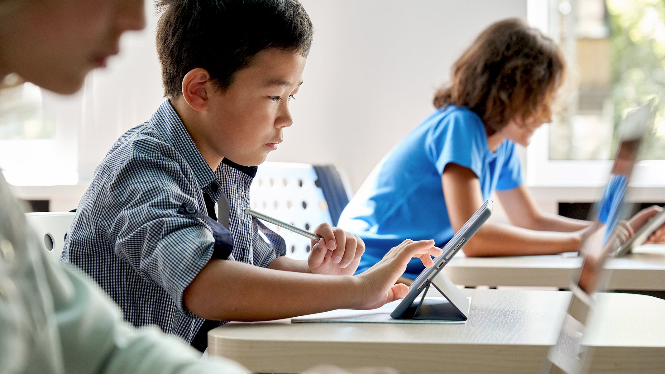 Una fila di studenti seduti ai loro banchi che utilizzano i tablet in un'aula moderna illuminata dal sole