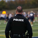A law enforcement officer standing on a football field watching the game