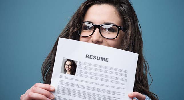 A smiling person holding a resume over the lower part of their face